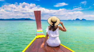 Happy traveler woman relaxing on boat near tropical island in Thailand