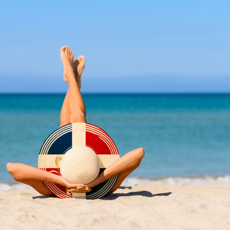 A woman relaxing on the beach in a straw hat in the colors of the Dominican flag