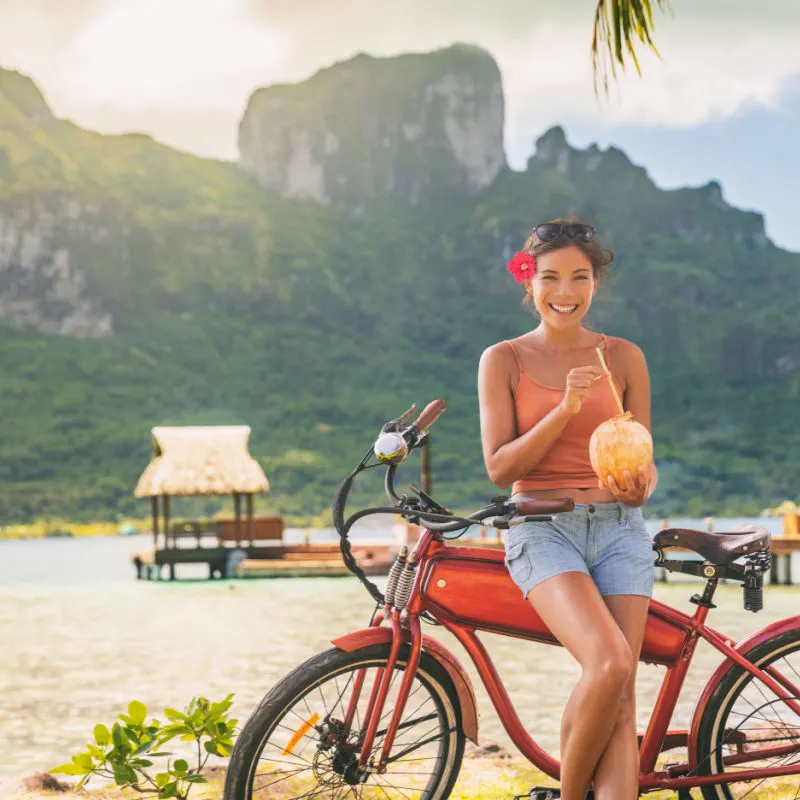 A woman cyclist takes a break to have a drink from a coconut while biking in Bora Bora