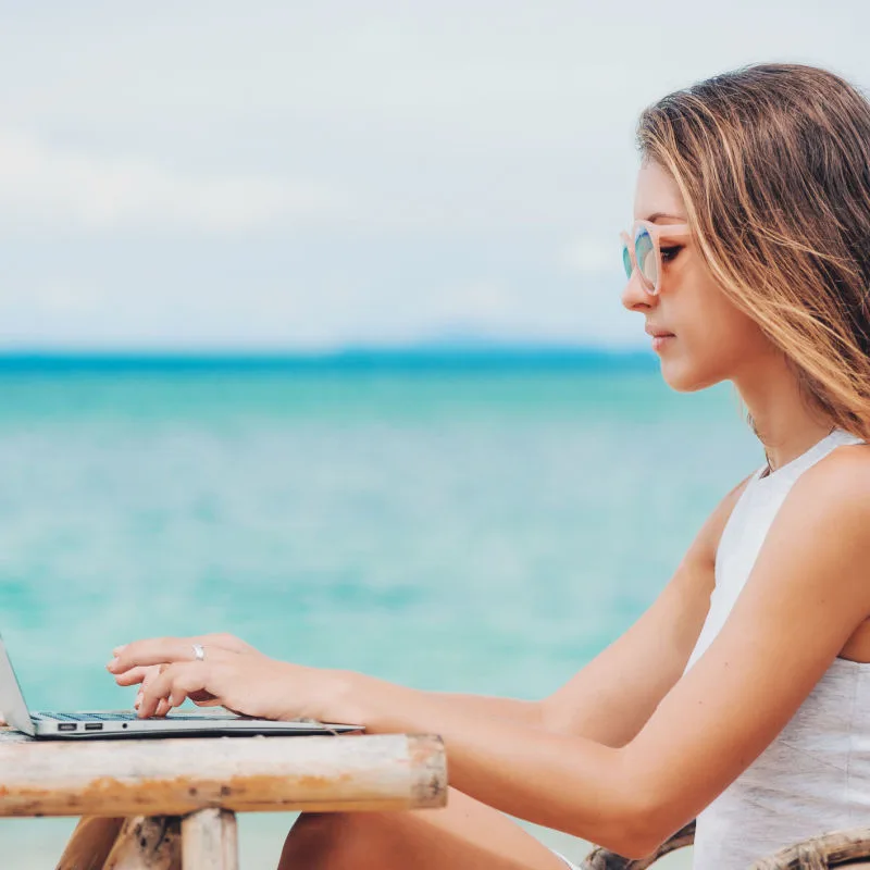 A woman works on a her laptop on a wooden table at the beach