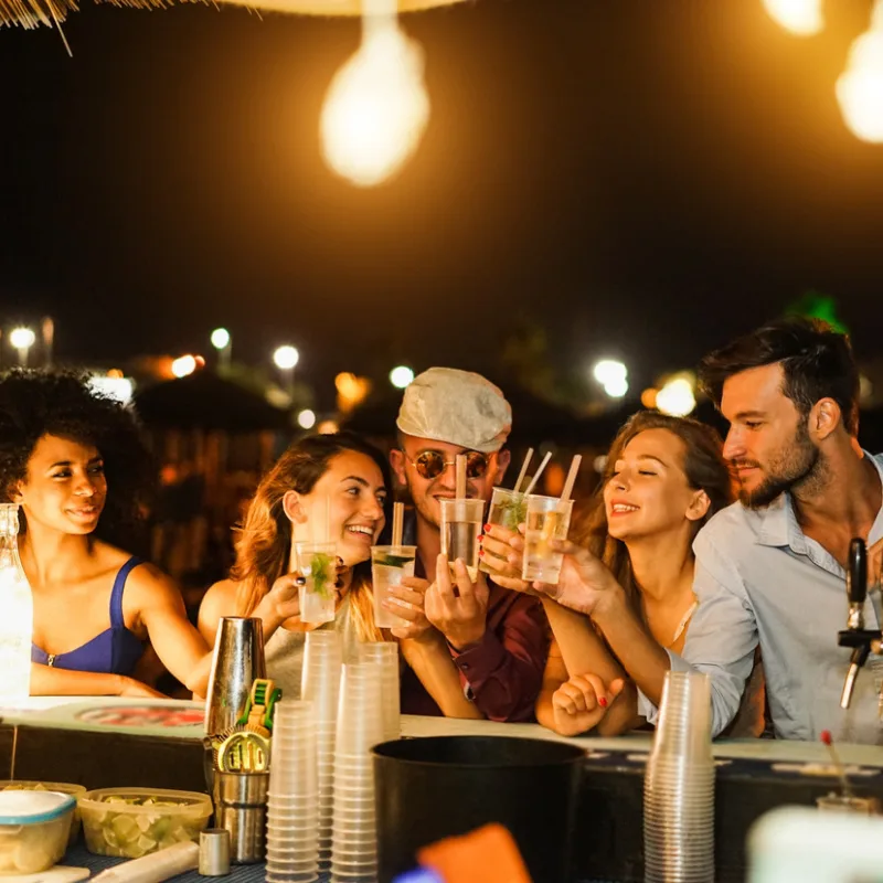 Friends At Beach Bar at Night Raising A toast With Their Cocktail Drinks