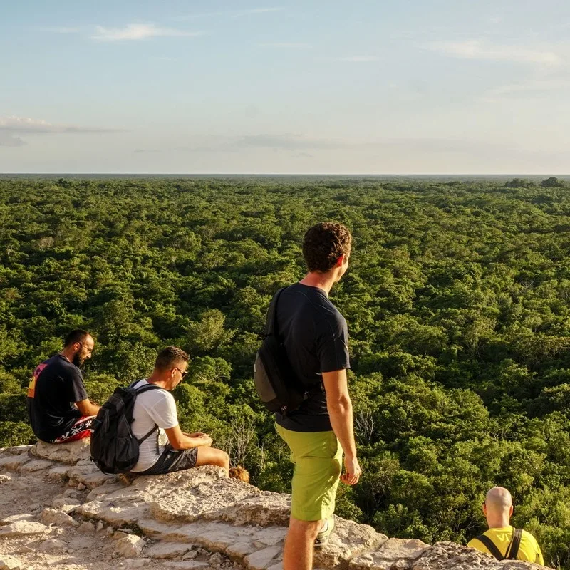 Group Of Tourists Stood Atop An Ancient Pyramid In Coba Overlooking The Jungle In The Yucatan Peninsula, Mexico