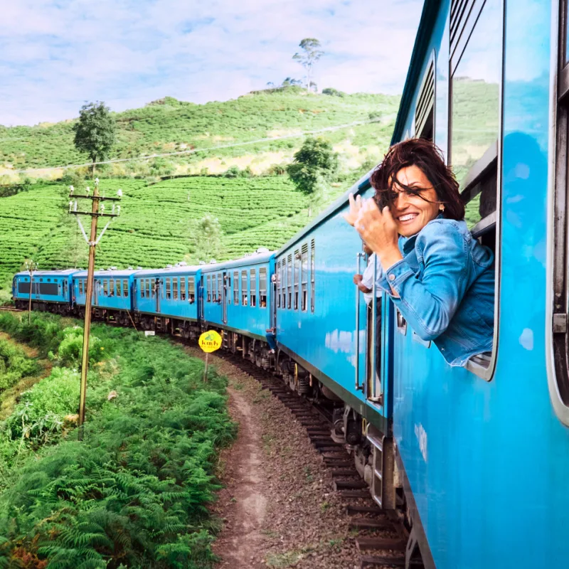 Happy Smiling Woman Looking Out From Window As She Travels In A Blue Train In Sri Lanka, South Asia