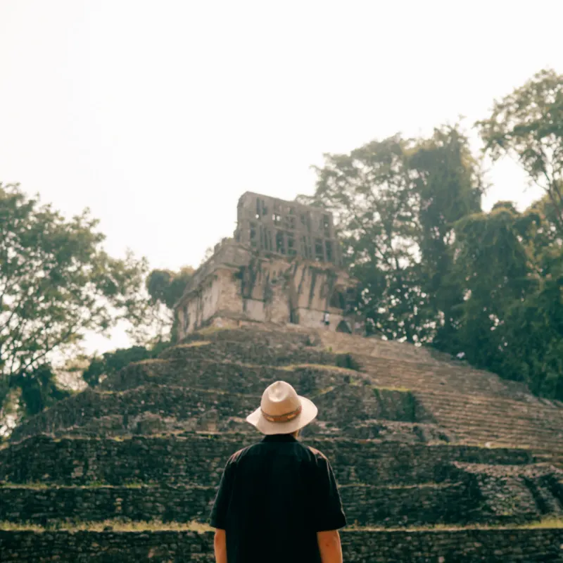 Hiker man with a hat looking at ancient Palenque Mayan ruins