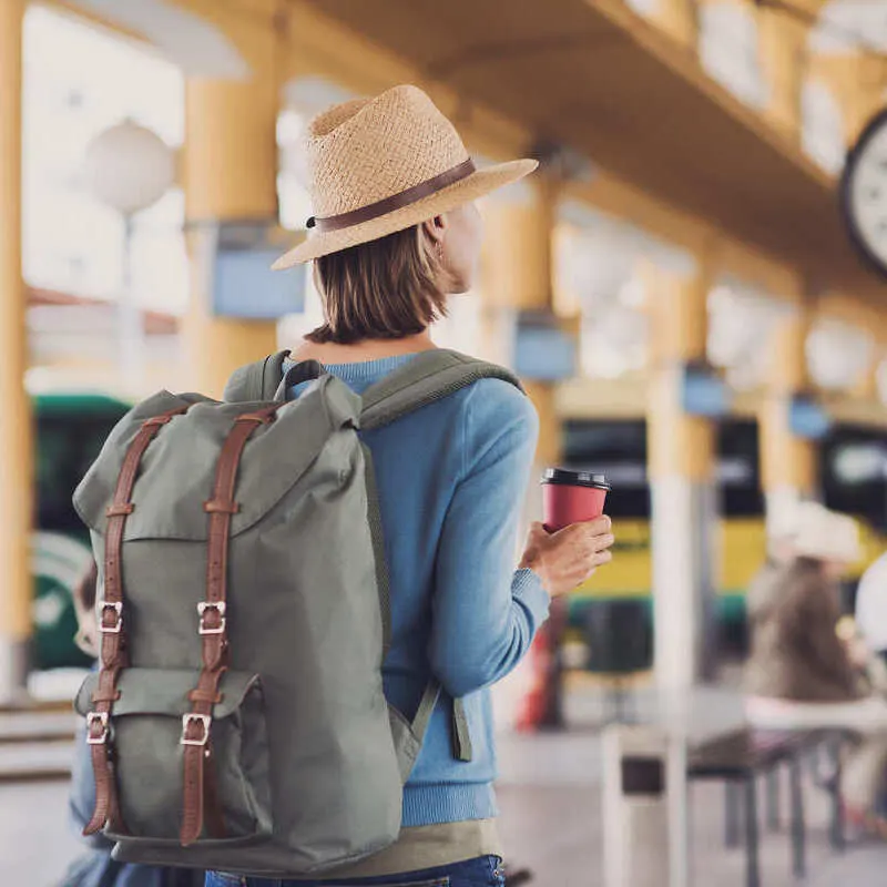 Young Backpacker Holding Her Coffee As She Waits For Her Train To Arrive To The Station, Unspecified Location