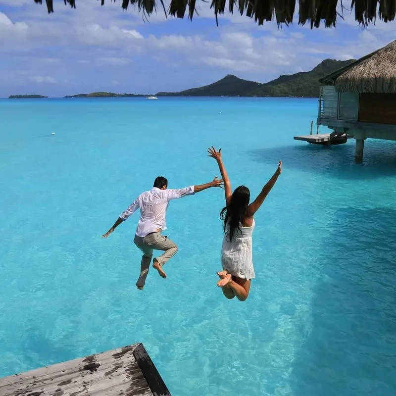 Young Couple Jumping Into The Ocean In Bora Bora, French Polynesia