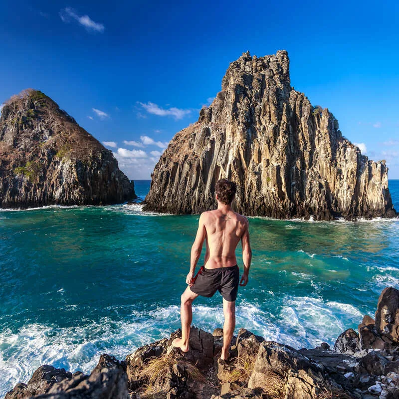 Young Male Watching The Twin Brothers Rock Formation In Fernando De Noronha, Pernambuco, Brazil