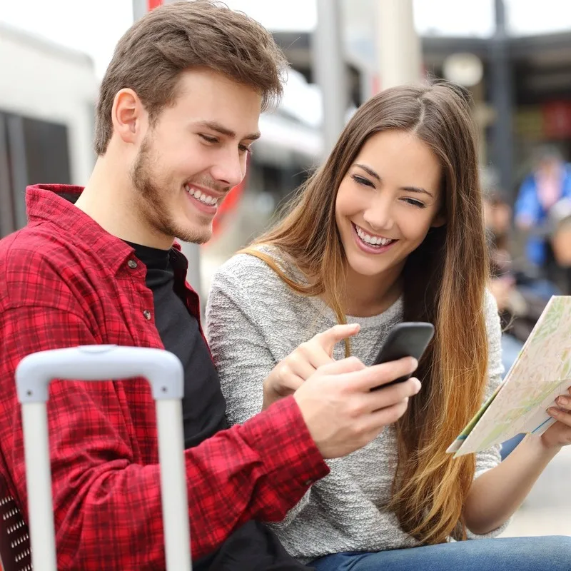 Young Smiling Couple Checking A Map In A Train Station Ahead Of Boarding, Unspecified Location